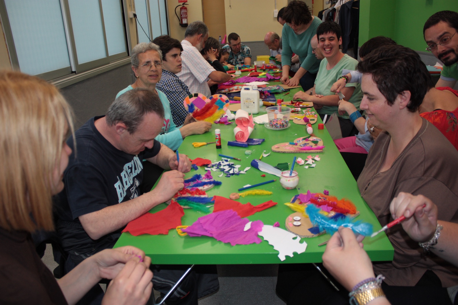 Participants fent manualitats al voltant d'una taula plena de papers de colors