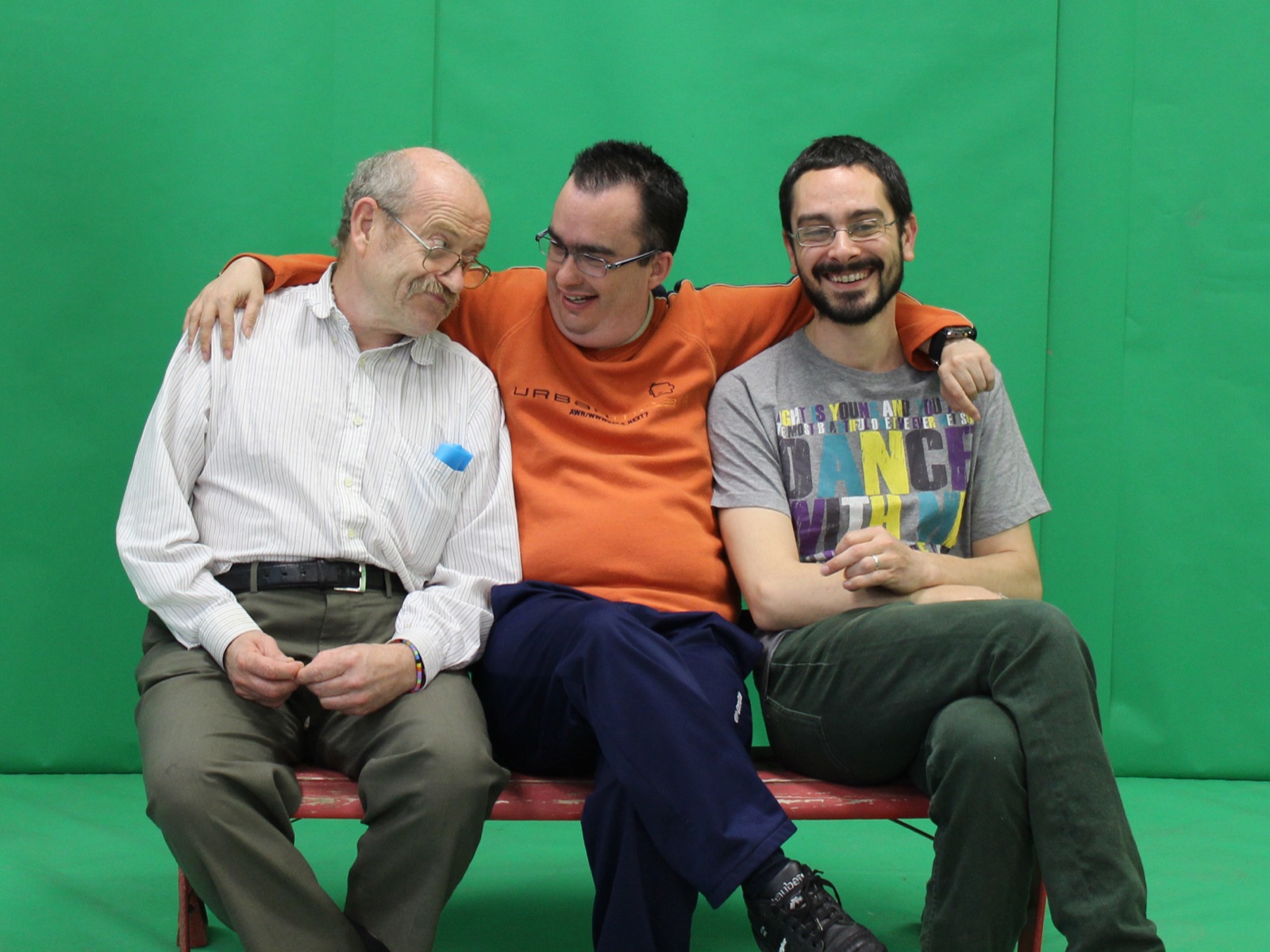 Tres participants asseguts en un banc, abraçats i somrients