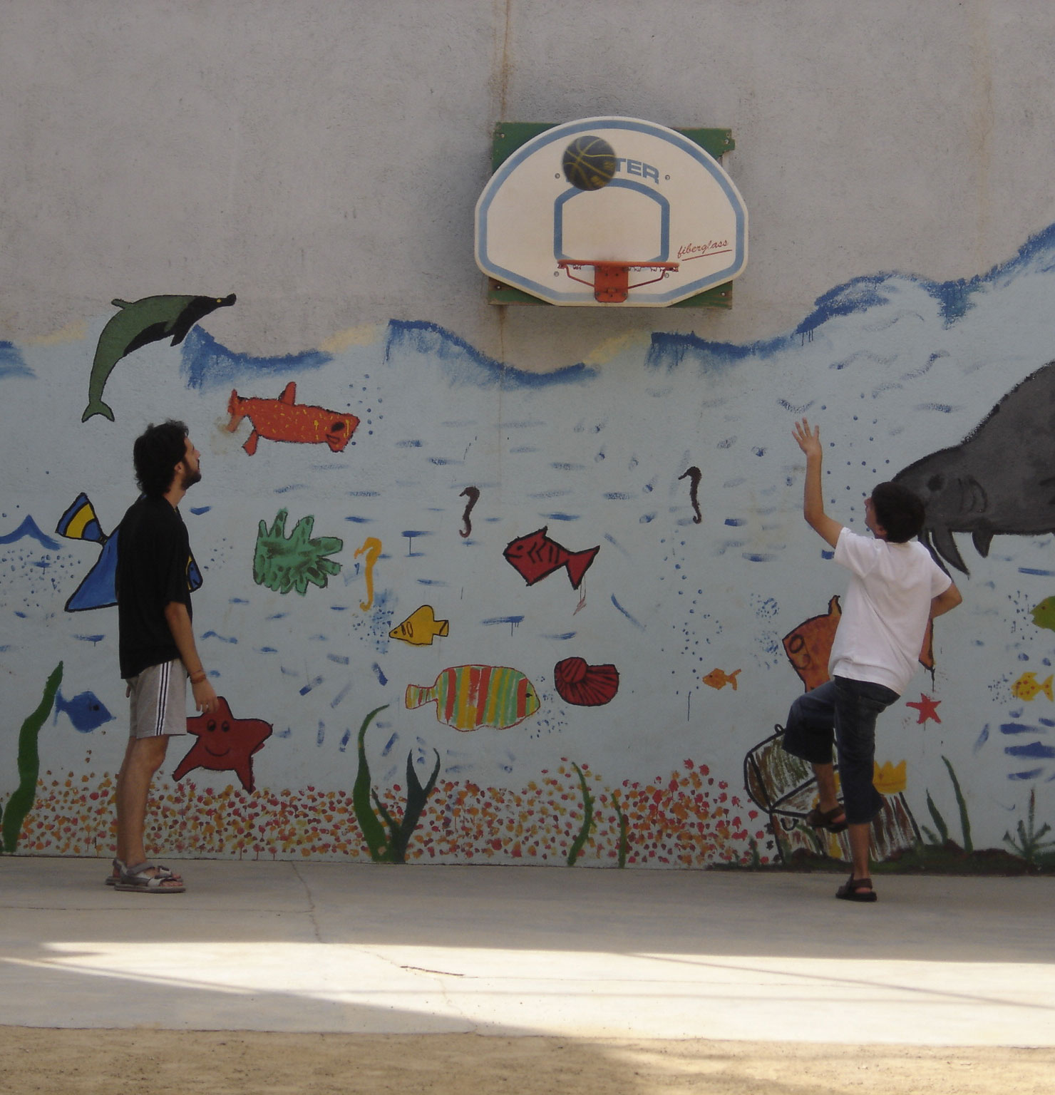 Dos infants jugant a bàsquet davant d'un mural de peixos